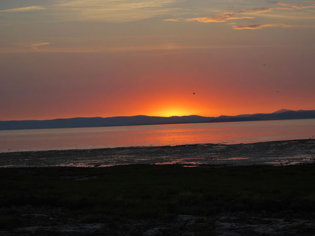 the sun sets with a sky fading from yellow to deep blue over distant hills