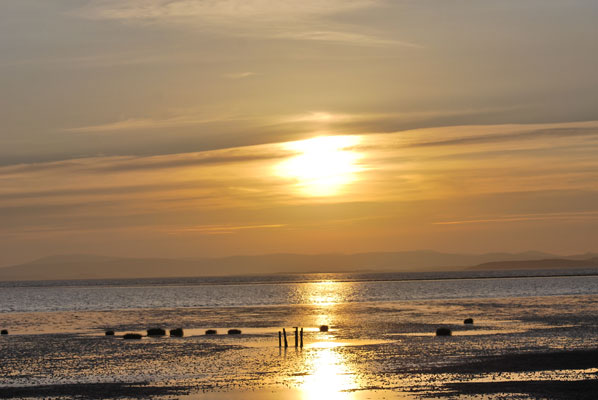 sunset over hest bank with hills in the distance and sunlight reflecting off of the water in the foreground