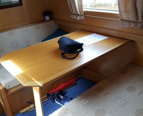 a bag sits on a table in the cabin of a narrowboat beneath the table are an umbrella and a single shoes