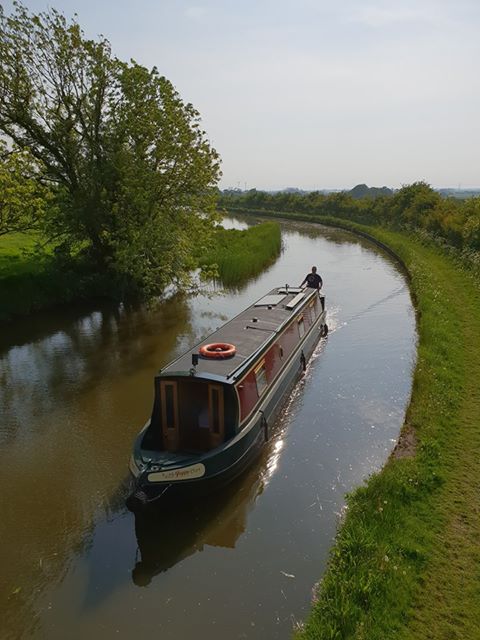 poppy the narrowboat rounding a broad curve in the lancaster canal in bright sunshine